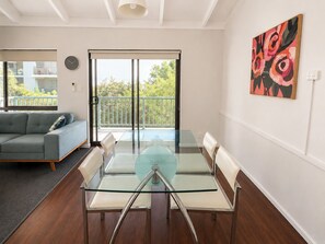 Un salon moderne avec une table à manger en verre, un canapé gris et un balcon offrant une vue sur la verdure.