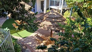 Una zona patio con una struttura a tetto di paglia, sedute e vegetazione circostante.