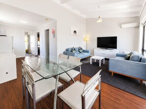 A modern living room with a glass dining table, two sofas, a flat-screen TV, and a white cabinet.