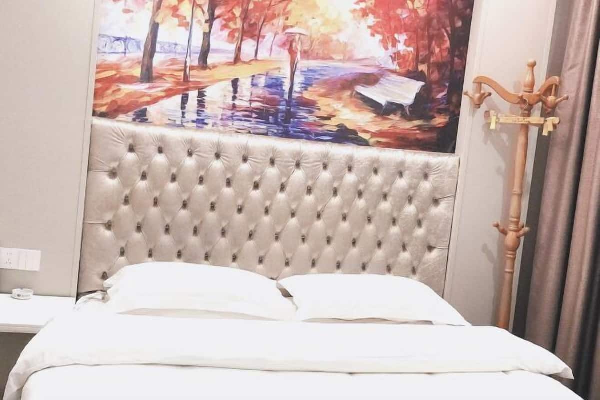 Ein Bett mit einem gepolsterten Kopfteil, ein Gemälde einer Parklandschaft und ein hölzerner Kleiderständer.