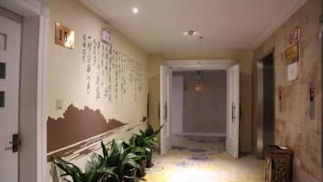 Un couloir d’hôtel avec un sol recouvert de moquette, des plantes en pot et un mur orné de texte et de chiffres.