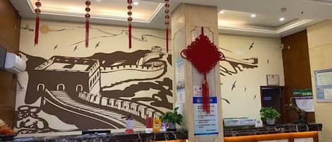A hotel reception area with a marble counter, a wall mural, and a red decorative hanging.