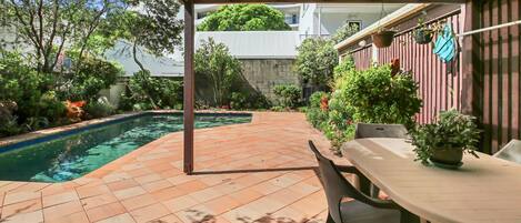 A covered patio area with a pool, outdoor seating, and potted plants.