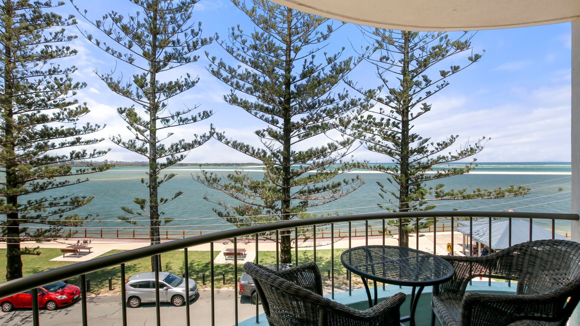 A balcony with wicker furniture overlooking a beach and ocean.
