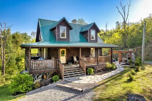 Une cabane en rondins avec un porche, un chemin de pierre et un espace extérieur aménagé pour s’asseoir.