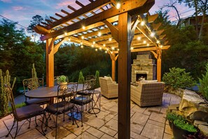 Une terrasse extérieure dotée d’une pergola, d’une cheminée en pierre et de mobilier d’extérieur.