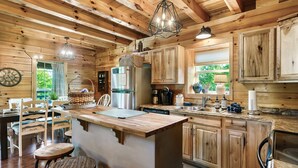 Interior de una cabaña de madera con una isla en la cocina, armarios de madera y un comedor con sillas y una mesa.