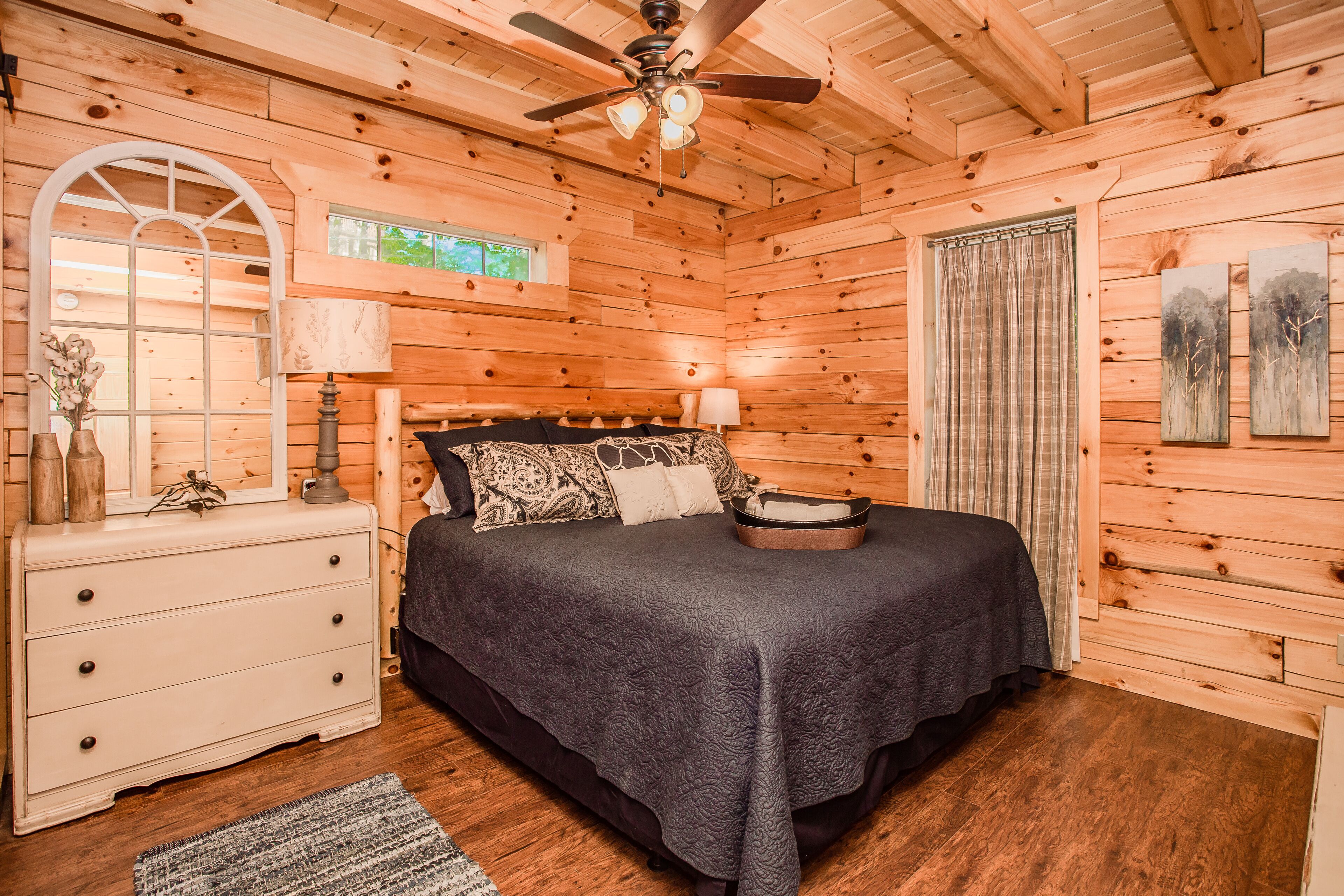 A wooden cabin bedroom with a bed, dresser, and ceiling fan.