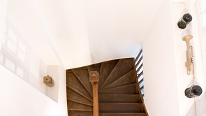 Un escalier en colimaçon avec une rampe en bois et des balustrades en métal, menant à un palier doté d’un mur blanc et d’une porte avec une poignée en laiton.