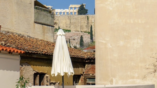 Une terrasse sur le toit, agrémentée d’un parasol blanc, de chaises longues en bambou et offrant une vue sur les bâtiments historiques en arrière-plan.