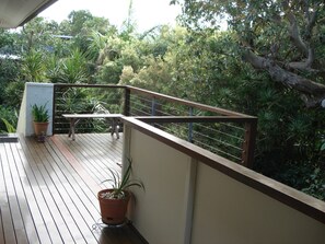 A wooden deck with a metal railing, surrounded by lush greenery and a variety of plants. - Two bedroom unit in fantastic location just above Deadmans Beach. (Point Lookout)