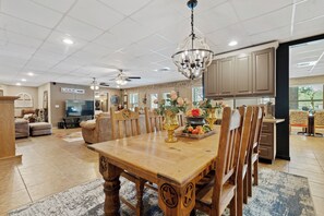 A spacious living room with a wooden dining table, comfortable seating, a chandelier, and a television.