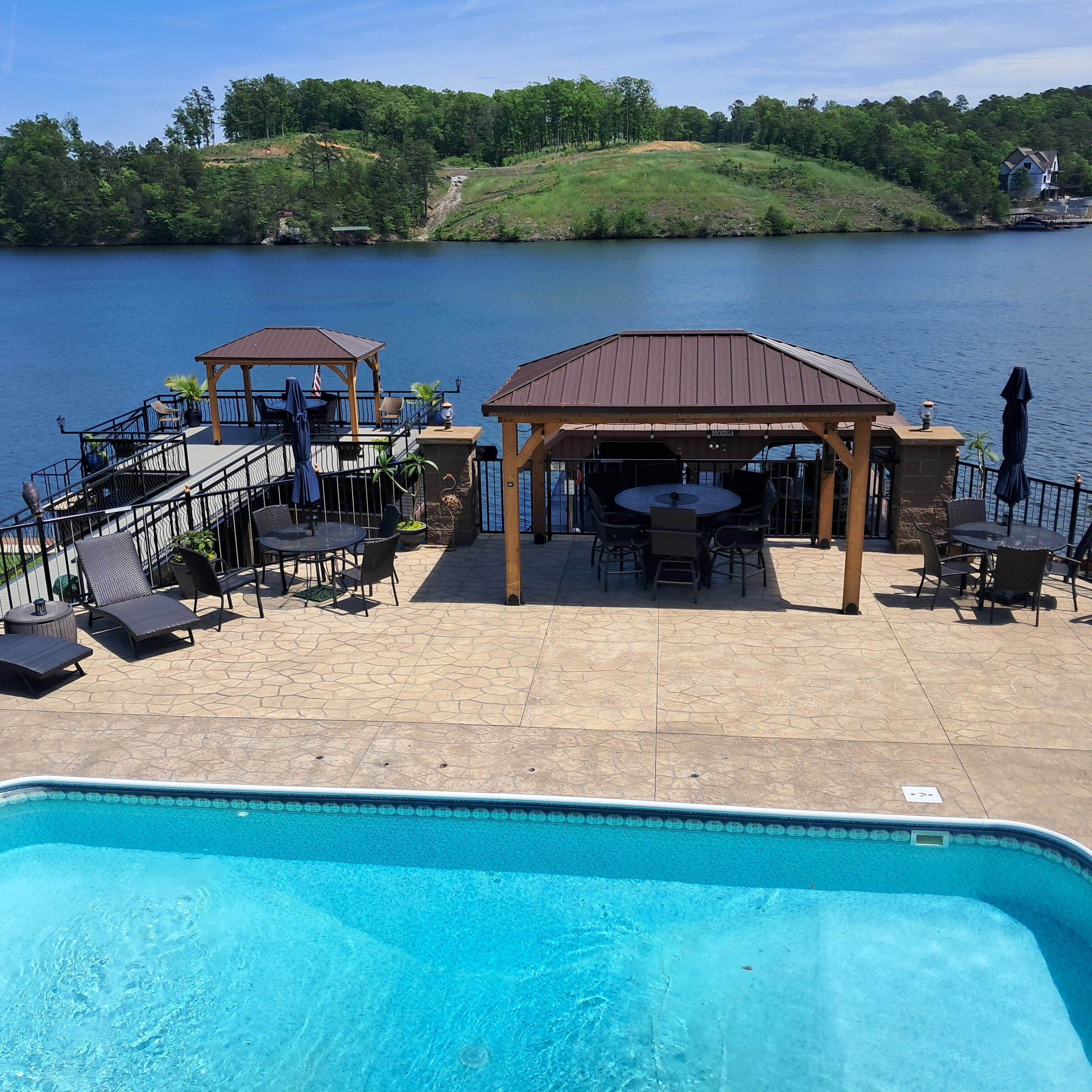 Un espace piscine agrémenté d’un gazebo, de chaises longues et offrant une vue sur un lac.
