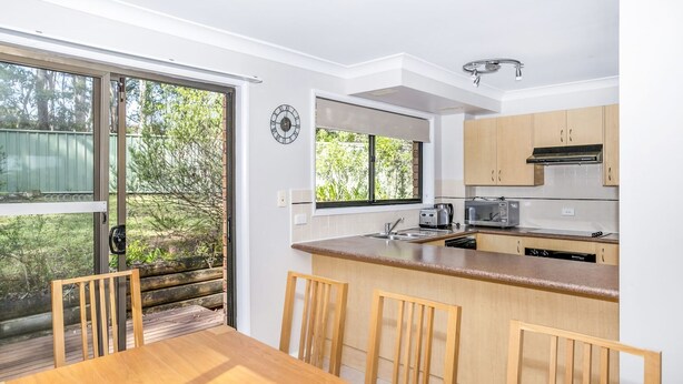 Una cocina moderna con una mesa y sillas de madera, horno empotrado y ventana con vista a la vegetación.