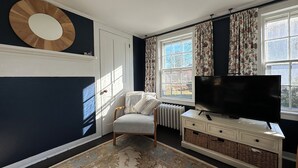 Een kamer met een grote televisie, een stoel, een radiator en een raam met gordijnen.