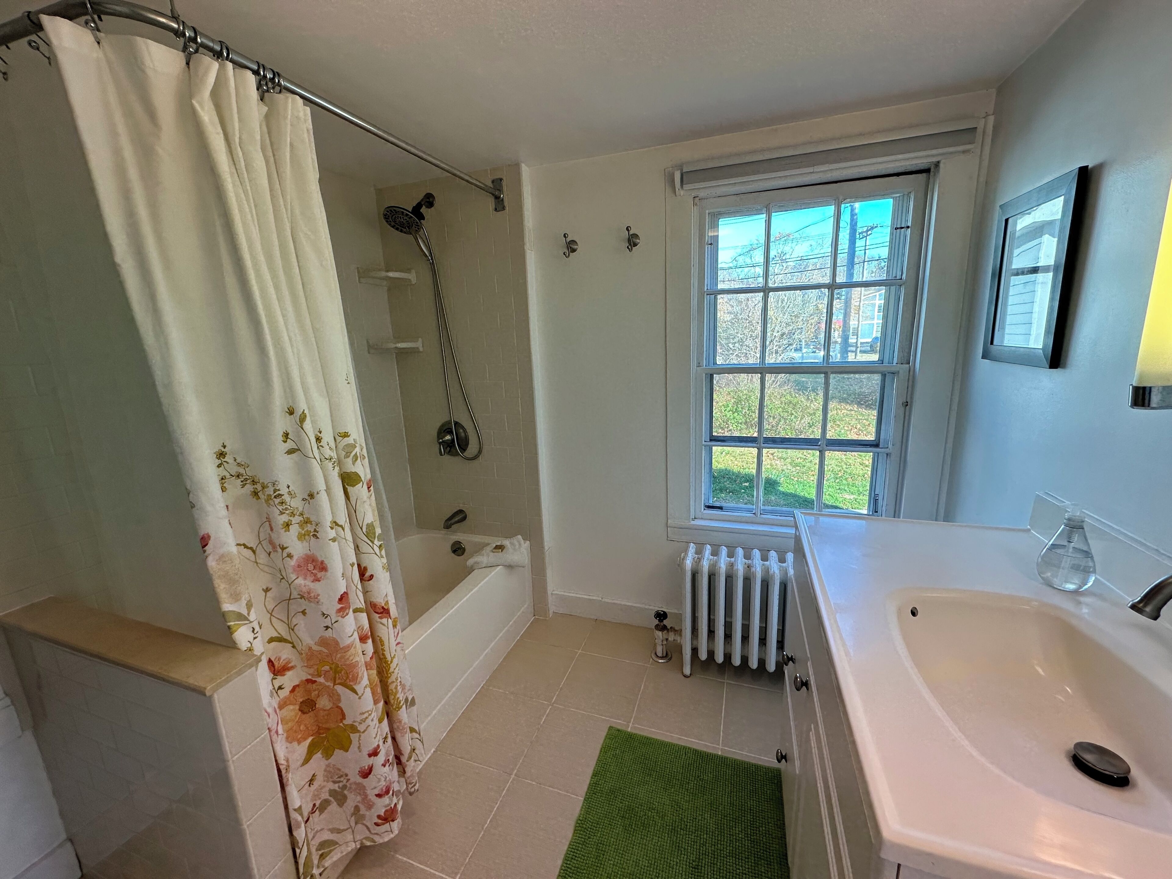 Un baño con ducha, bañera, ventana, lavamanos y radiador.