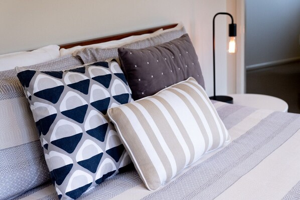 Una cama con una colcha a rayas y tres almohadas con diseños geométricos y a rayas.