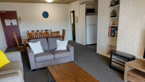 Un salon avec un canapé gris, des chaises en bois, une table basse en bois et une bibliothèque remplie de livres.