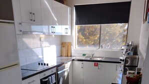 Une cuisine moderne avec des meubles blancs, un plan de travail noir, une fenêtre donnant sur les arbres et un four noir.