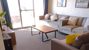 Un salon comprenant un canapé, une table basse et un divan. Une porte-fenêtre coulissante donne accès à un espace extérieur.