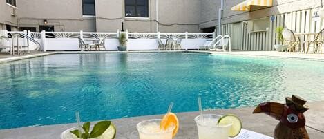Une piscine avec des chaises longues et des parasols, et trois boissons sur une table.