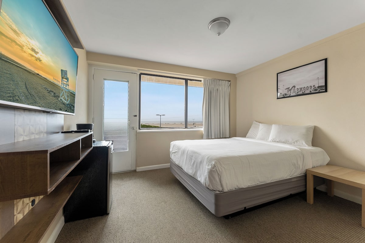 Een hotelkamer met een bed, een televisie, een bureau en een raam met uitzicht op het strand.