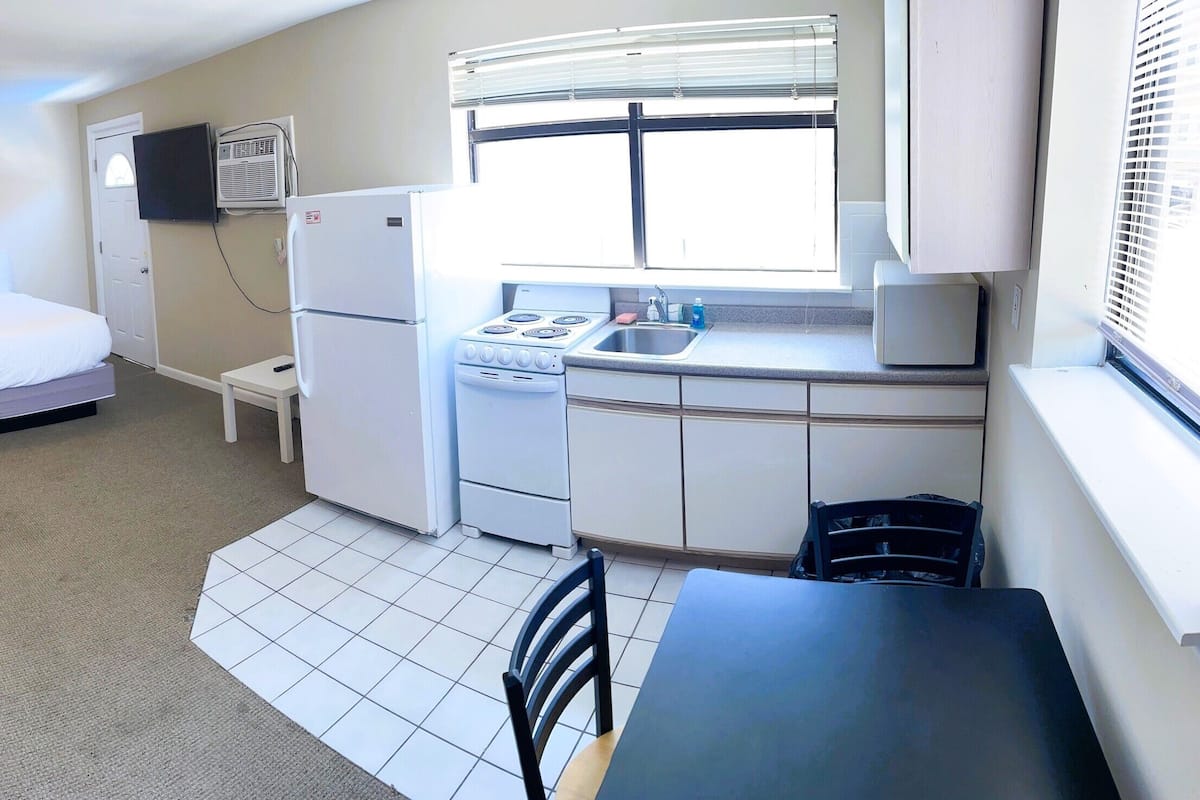 Een compacte hotelkamer met twee eenpersoonsbedden, een kitchenette met fornuis en spoelbak, een klein tafeltje en een bank.