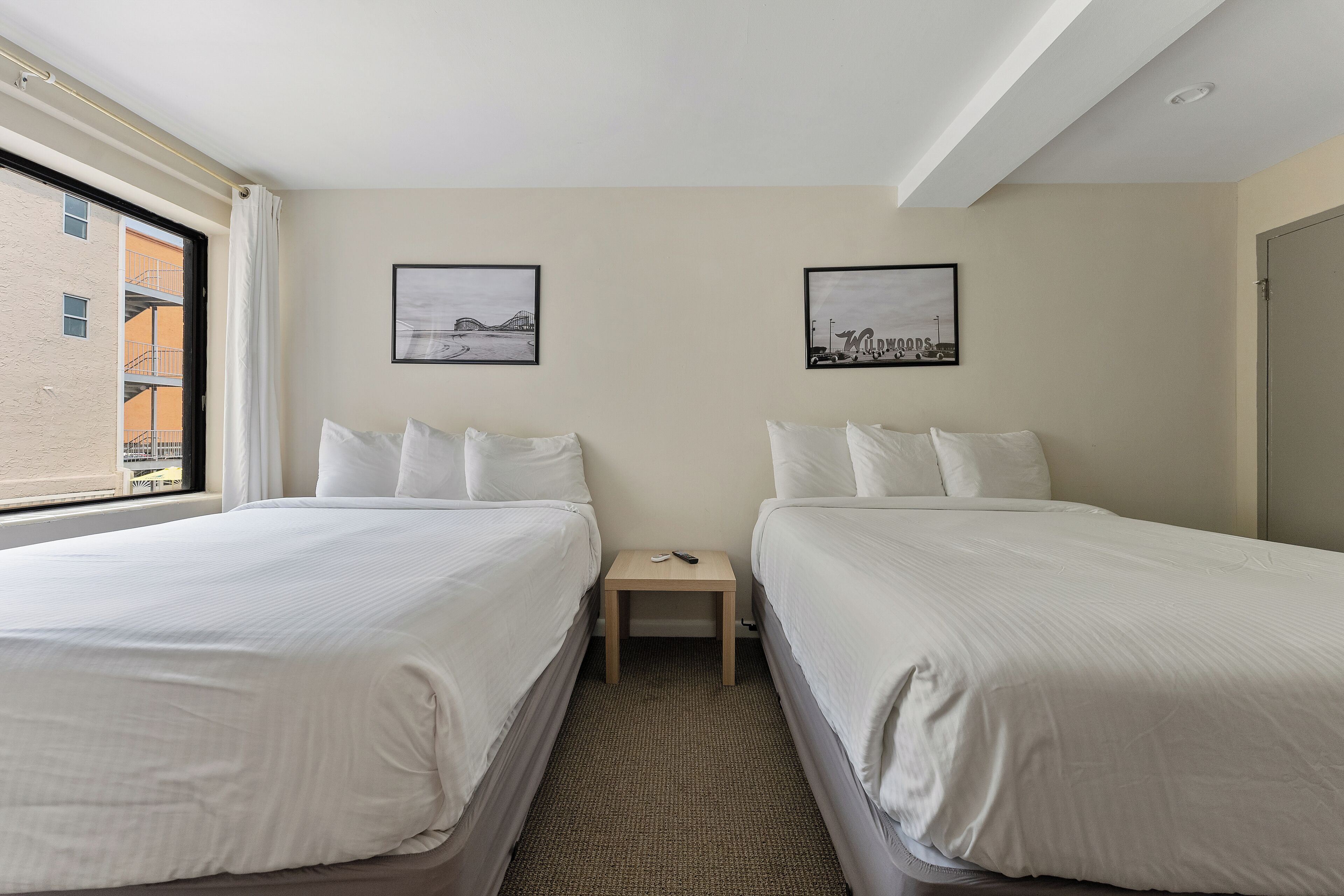 Una habitación de hotel con dos camas, una mesita y dos cuadros en la pared.