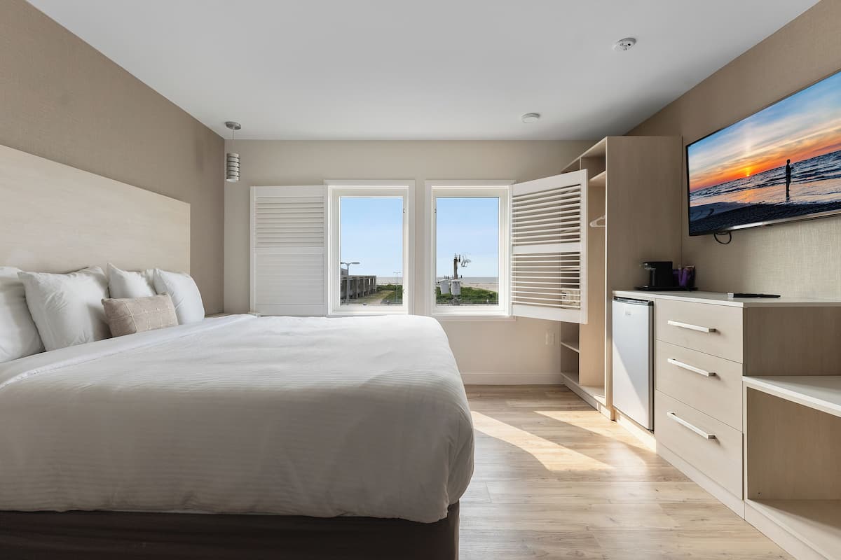 Een moderne slaapkamer met een groot bed, een televisie en uitzicht op de ondergaande zon door de ramen.