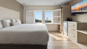 A modern bedroom with a large bed, a TV, and a view of the sunset through the windows.