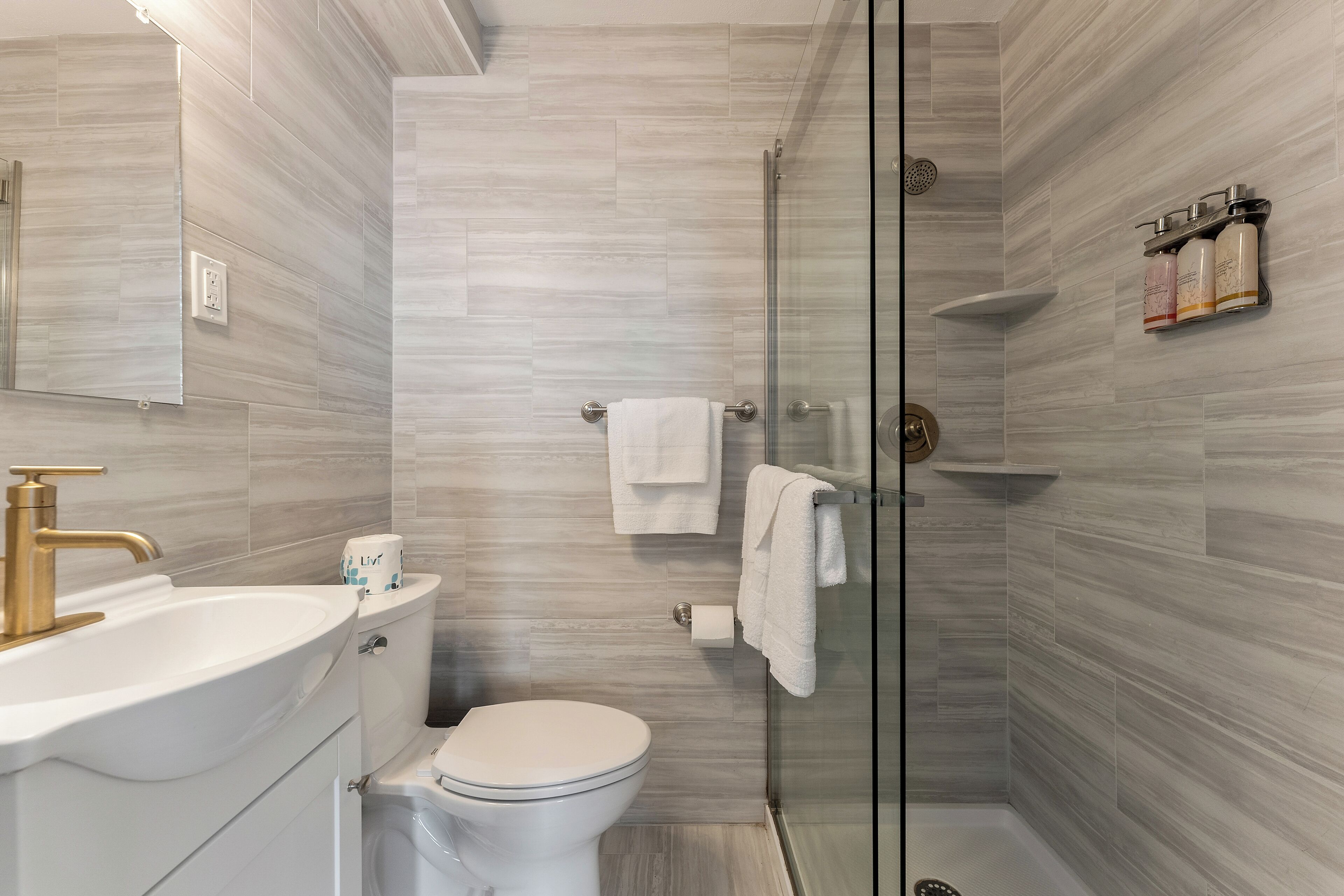 Un baño moderno con cabina de ducha de vidrio, lavamanos blanco y un inodoro.