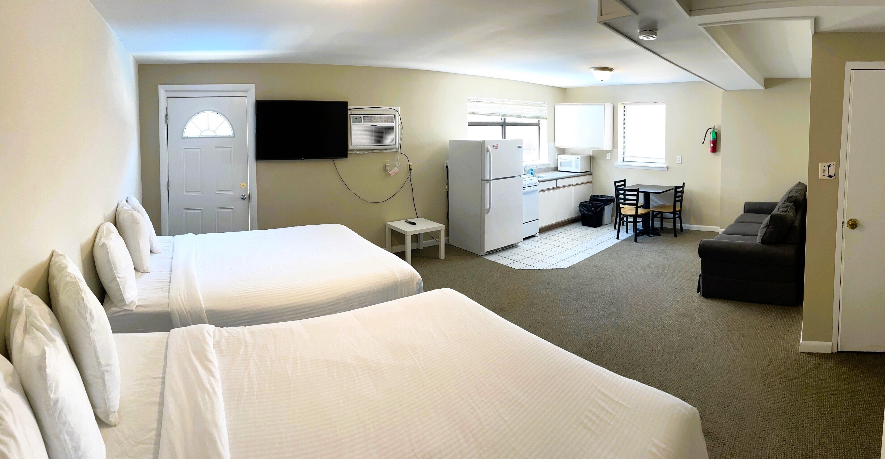 A hotel room with two beds, a kitchenette, a television, and a sofa.