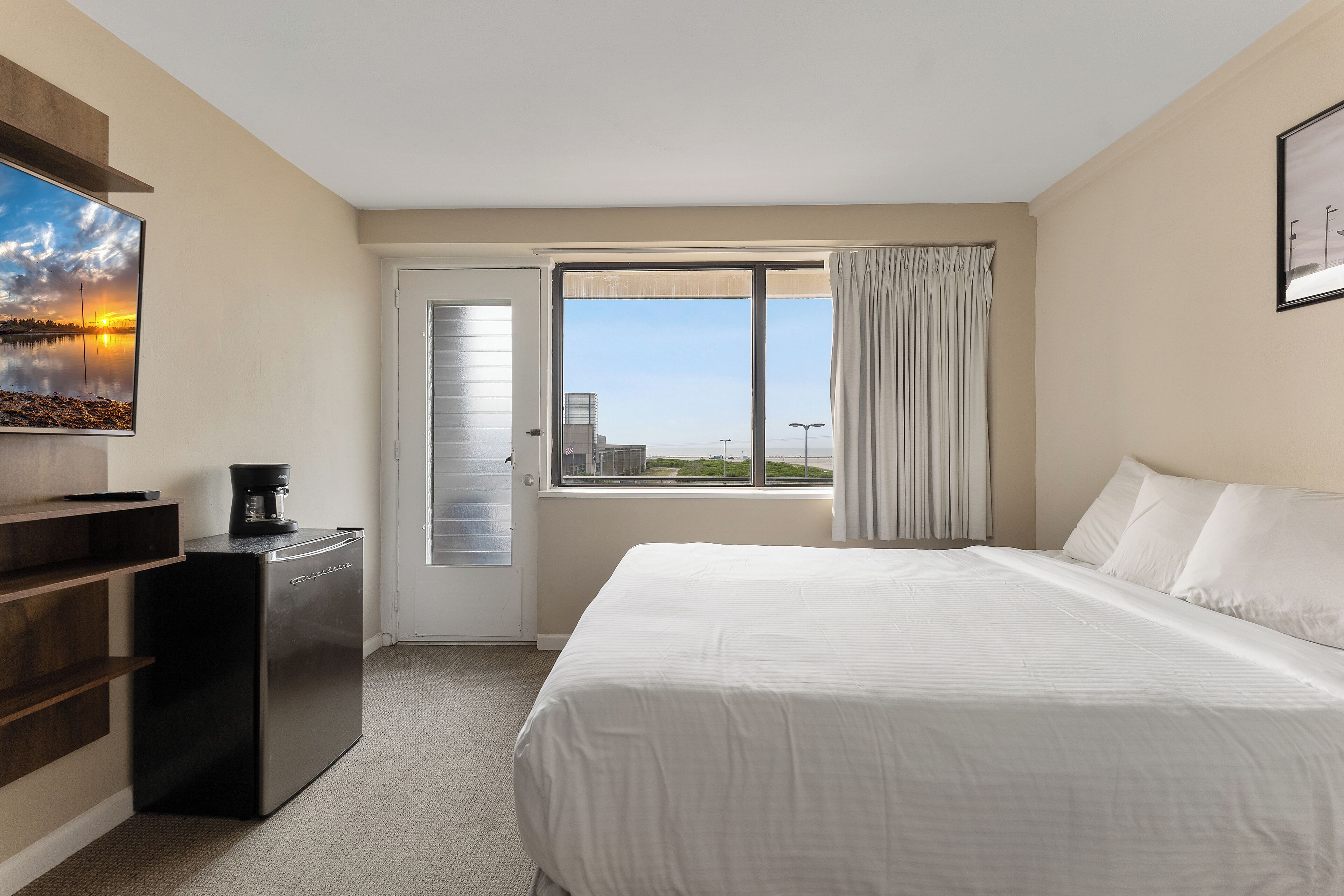 A hotel room with a bed, a desk with a coffee maker, a TV, and a window with a city view.