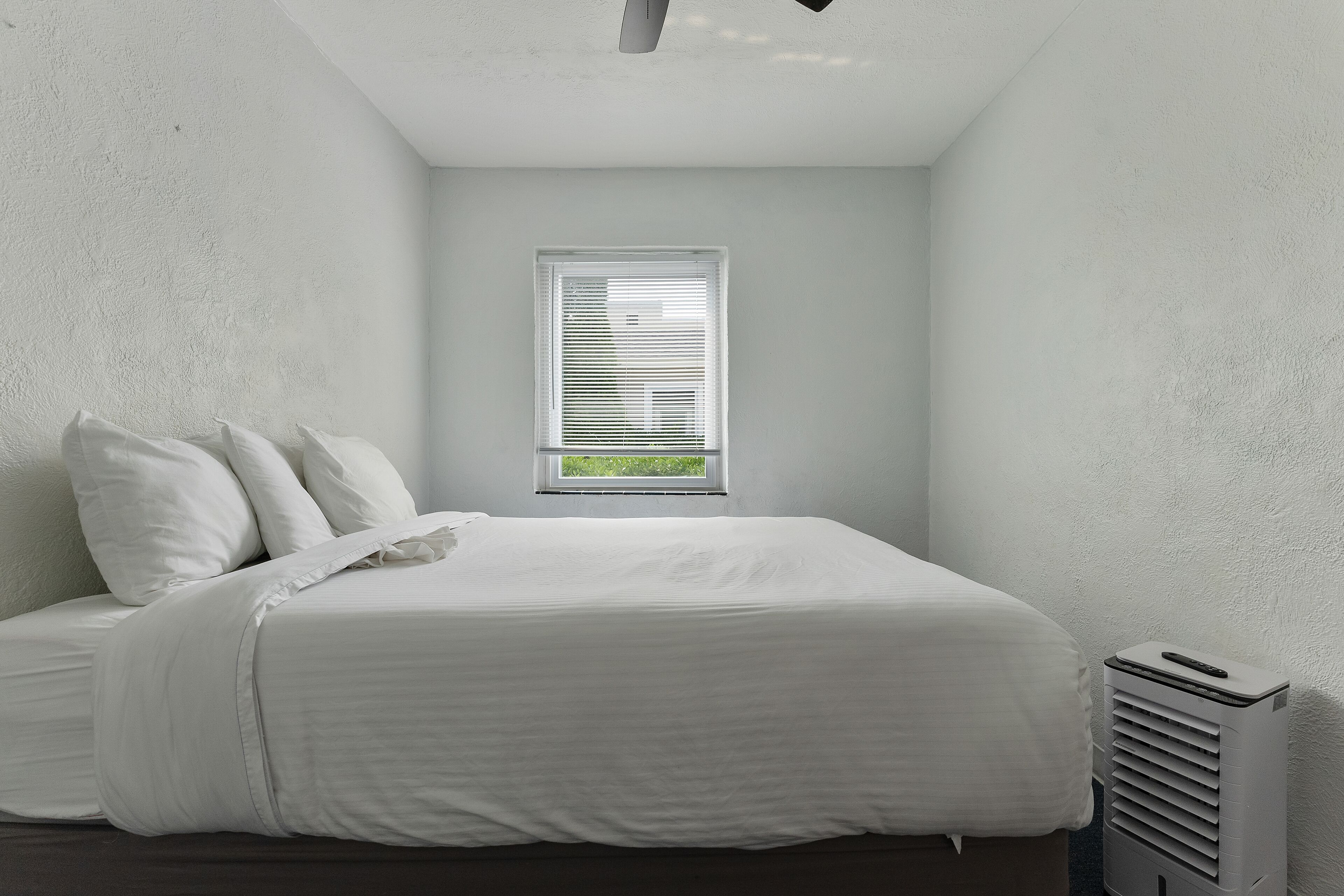 A bedroom with a bed, white walls, a window, and a radiator.