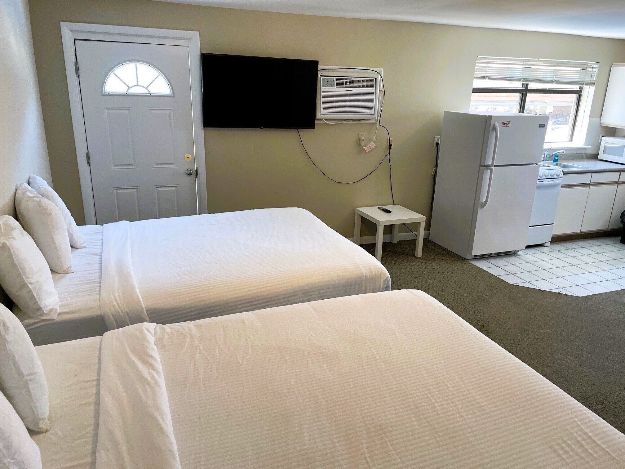 A hotel room with two beds, a TV mounted on the wall, a refrigerator, and a microwave.