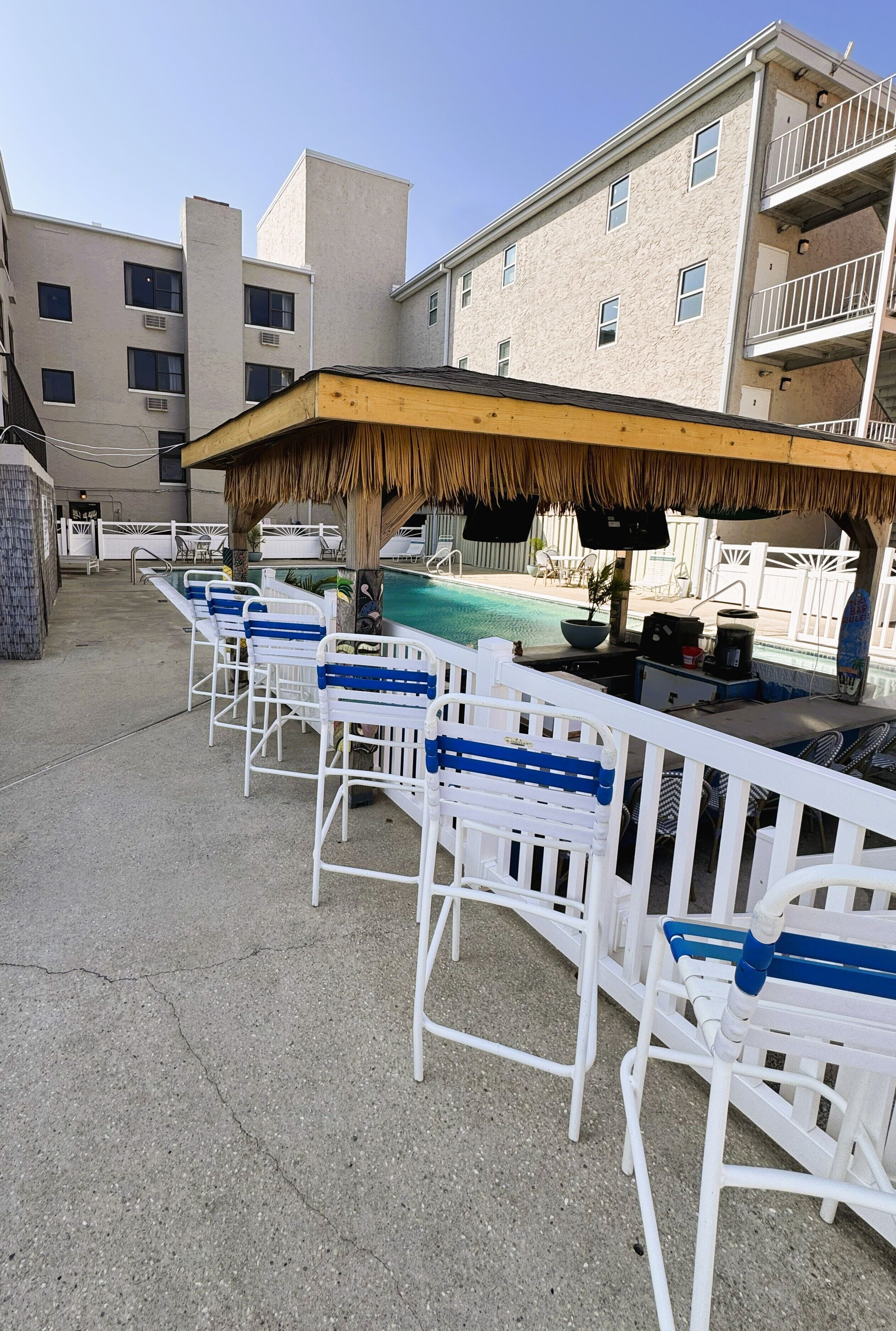 A poolside area with white chairs, a bar, and a thatched roof.
