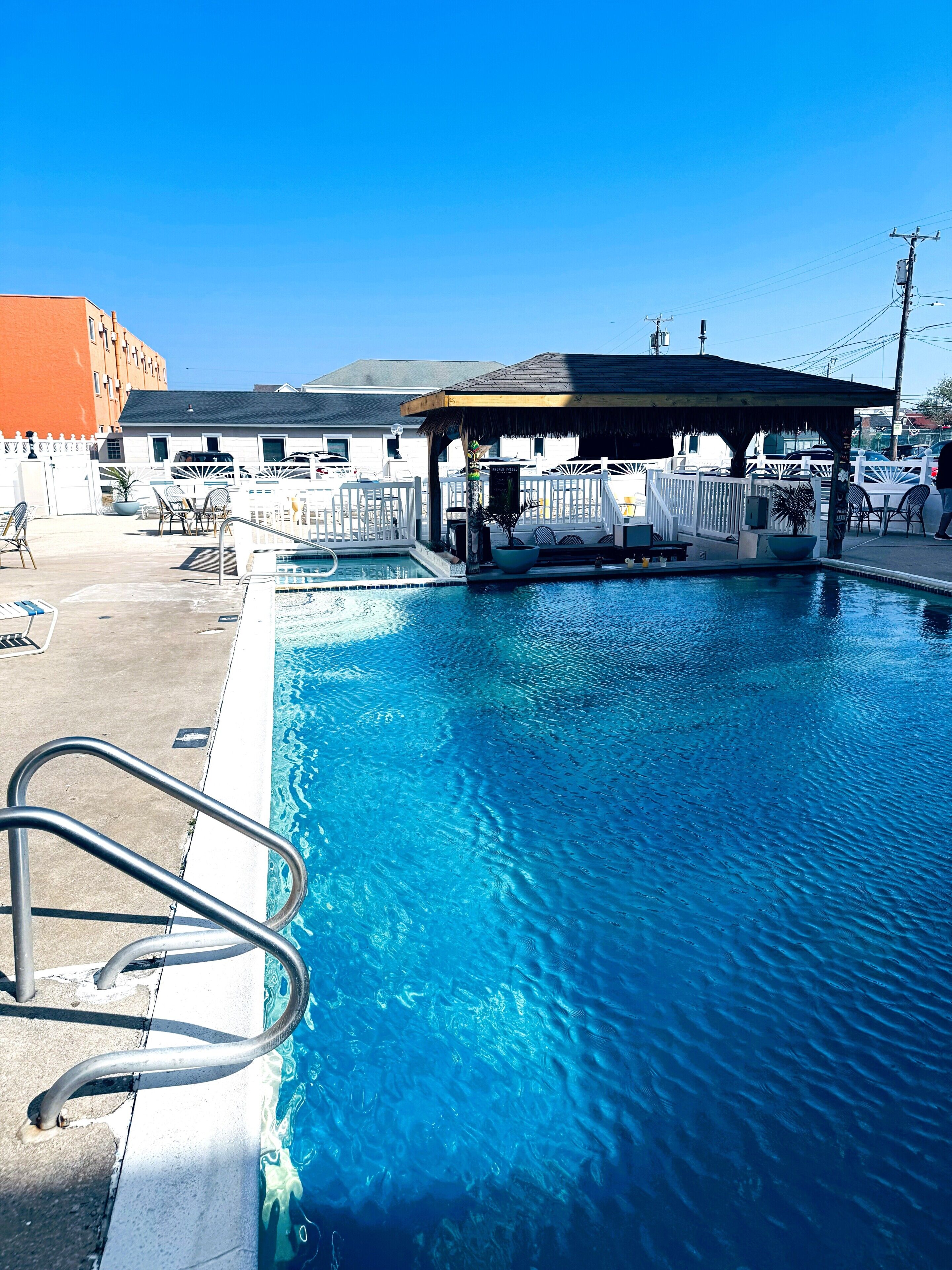 A swimming pool with a metal ladder, a covered seating area, and a white fence.