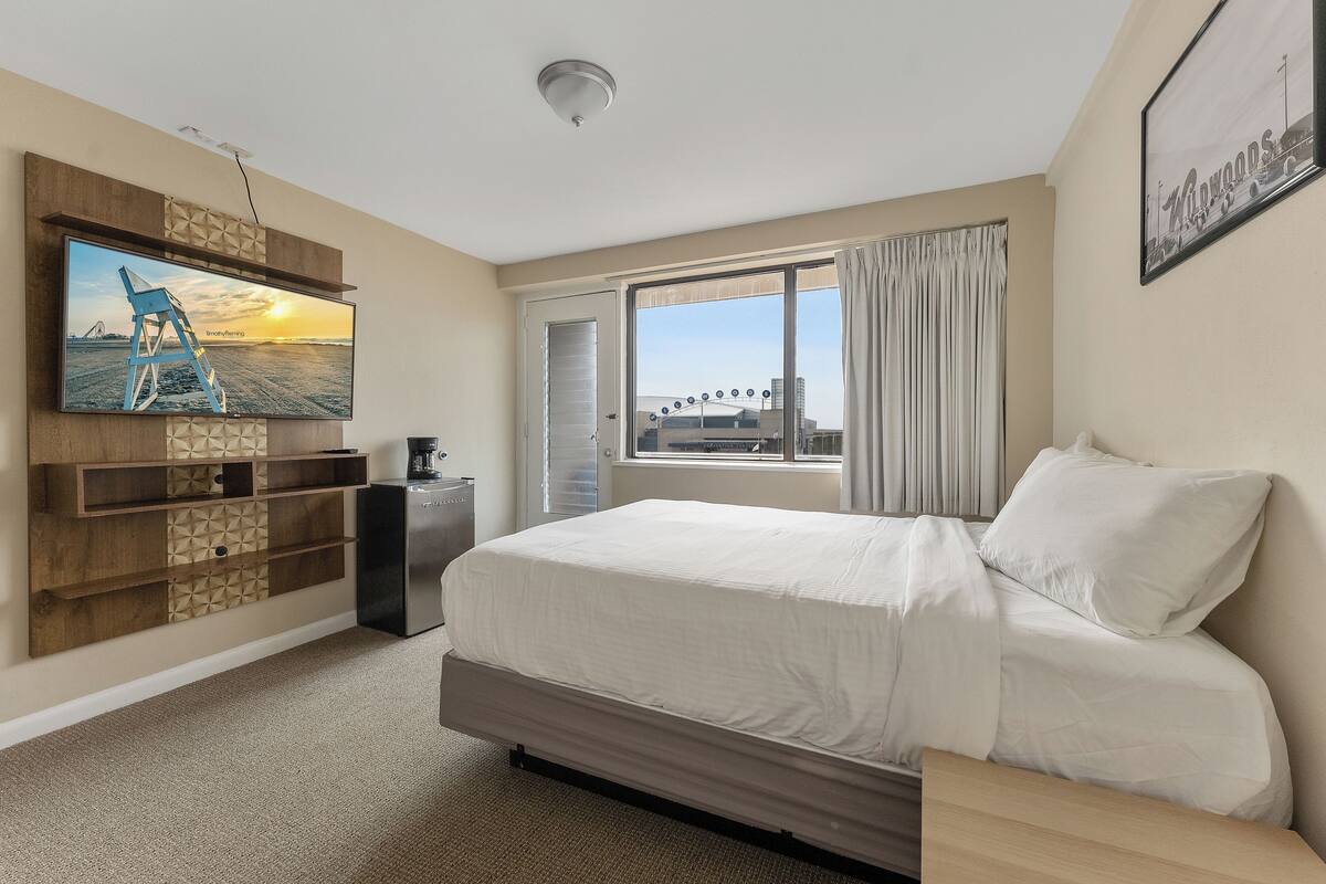 Een hotelkamer met een groot bed, een flatscreen televisie aan de muur, een klein bureau en een raam met uitzicht op de stad.