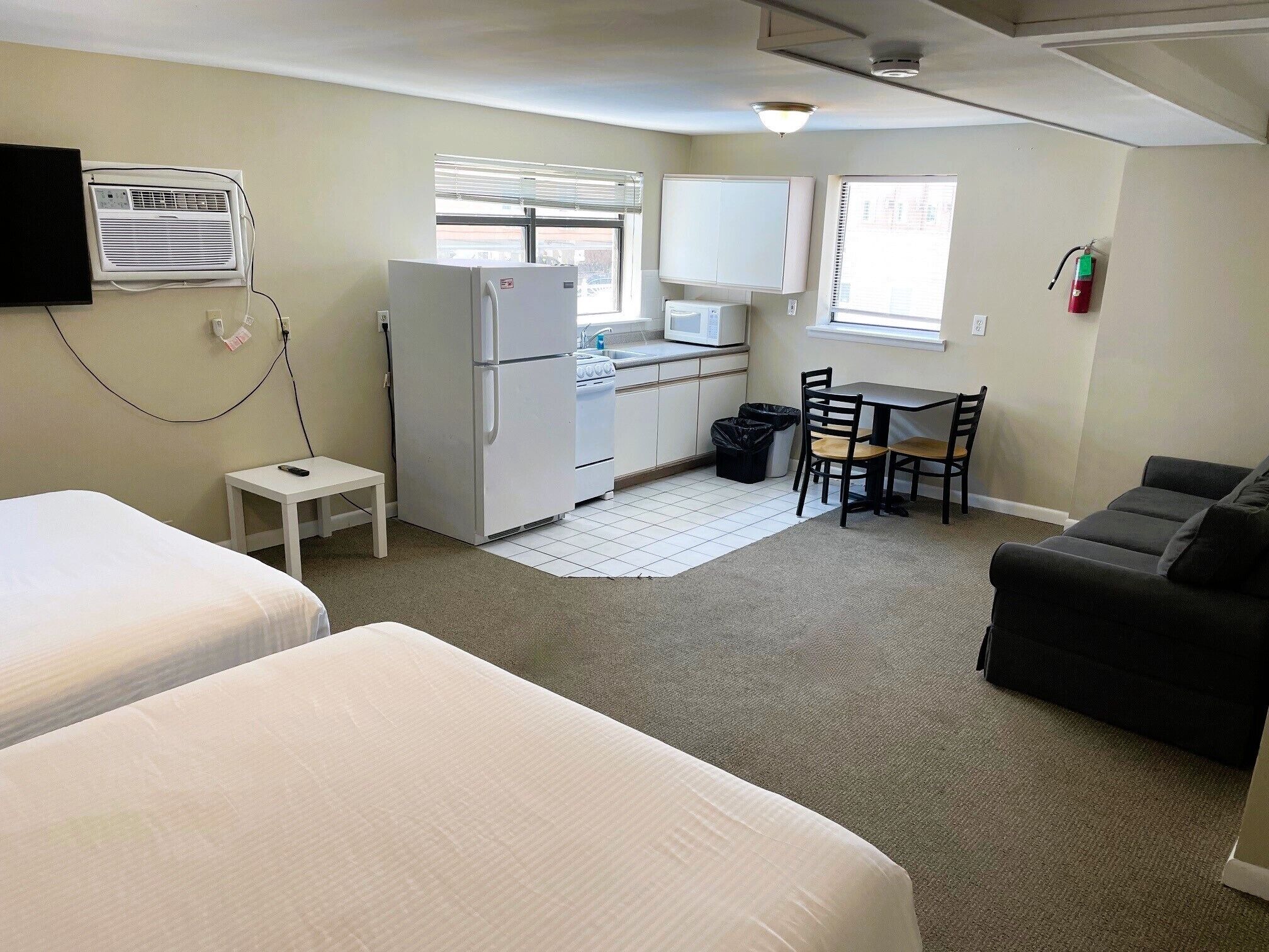 A compact hotel room with two beds, a kitchenette, a dining area, and a living space.