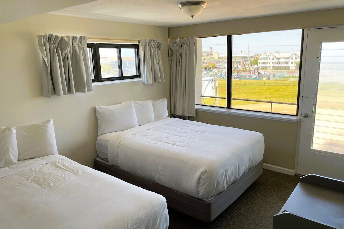 Een hotelkamer met twee bedden, een groot raam met uitzicht op de stad en een deur naar buiten.