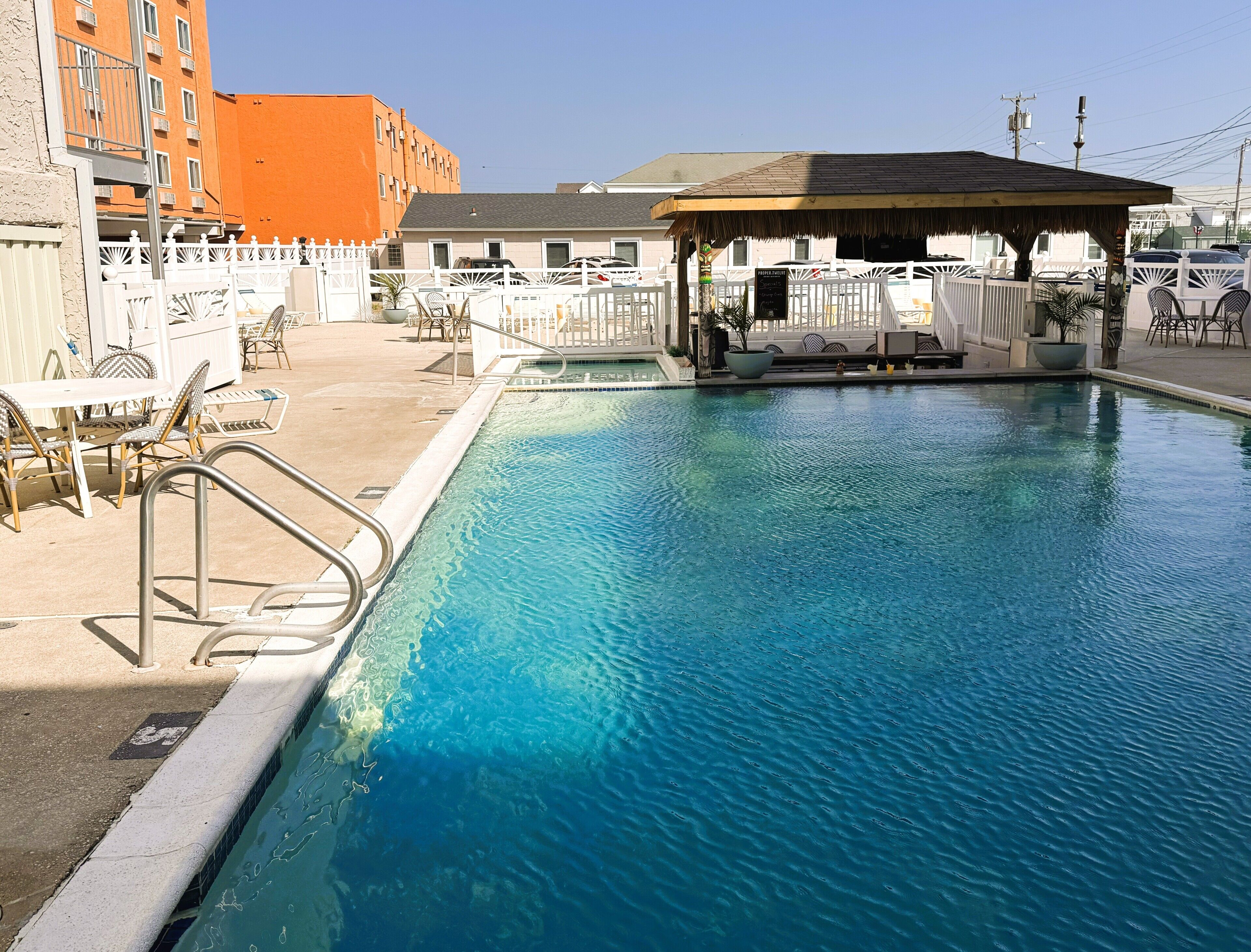A swimming pool with a covered seating area, lounge chairs, and a fenced patio.