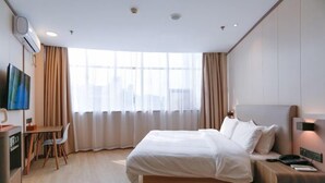 Quarto de hotel com cama, mesa de cabeceira, luminária, televisão e escrivaninha com cadeira.