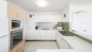 Eine kleine Küche mit weißen Schränken, einem Backofen, einer Spüle und einer Kaffeemaschine.