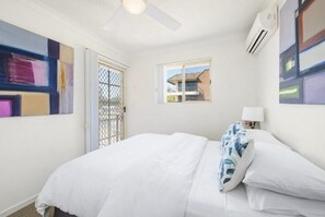 A hotel room with a bed, a window, an air conditioning unit, and artwork on the walls. - Seabreeze 4 on Lawson Street (Byron Shire)