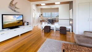A modern living room with a flat-screen TV, wooden flooring, and a view of the balcony. - 3 bedroom 2 bathroom spacious unit with water views. (Point Lookout)