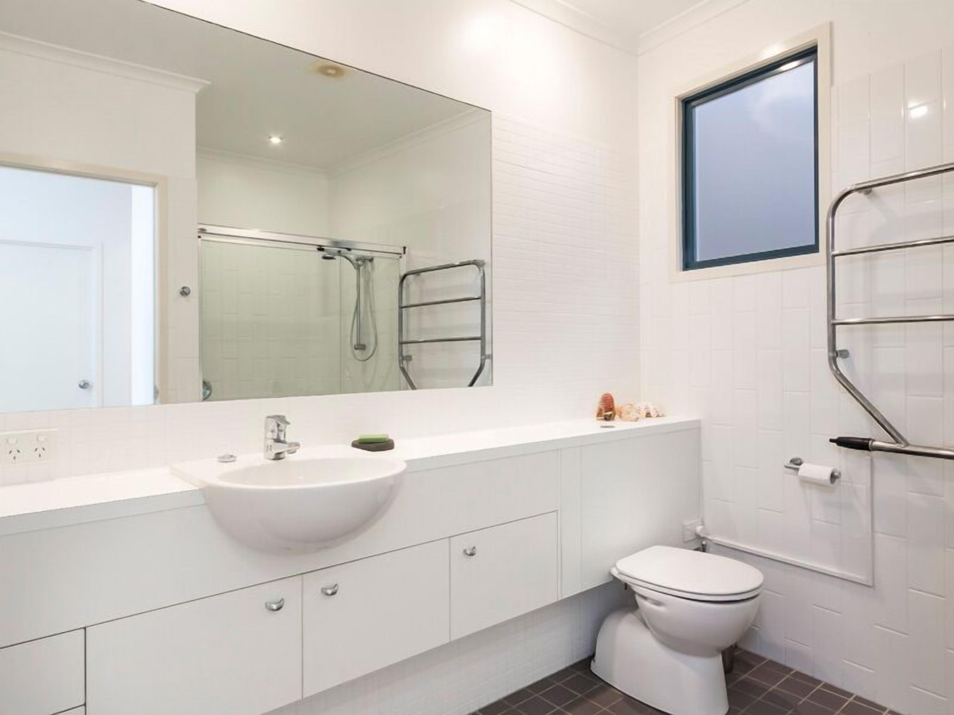 A modern bathroom with a white sink, mirror, and toilet.