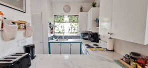 A kitchen with white cabinets, a stove, a microwave, and a window with a view of greenery. - Fully A/C Ground-Floor Oasis Steps from the Pool & South Coast (Bridgetown)