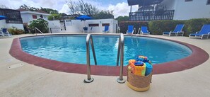 Piscina com escadas de metal, cadeiras de descanso e um cesto com toalhas coloridas.
