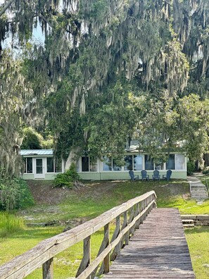 A wooden boardwalk leading to a building with a green roof, surrounded by trees with Spanish moss. - Lake living close to Gainesville, UF Health and University of Florida (Melrose)