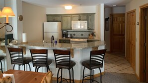 A kitchen with a central island, bar stools, a refrigerator, a microwave, and a coffee maker. - Ski In - Ski Out Condo in OberTal 'F' Building! (Stratton Mountain)